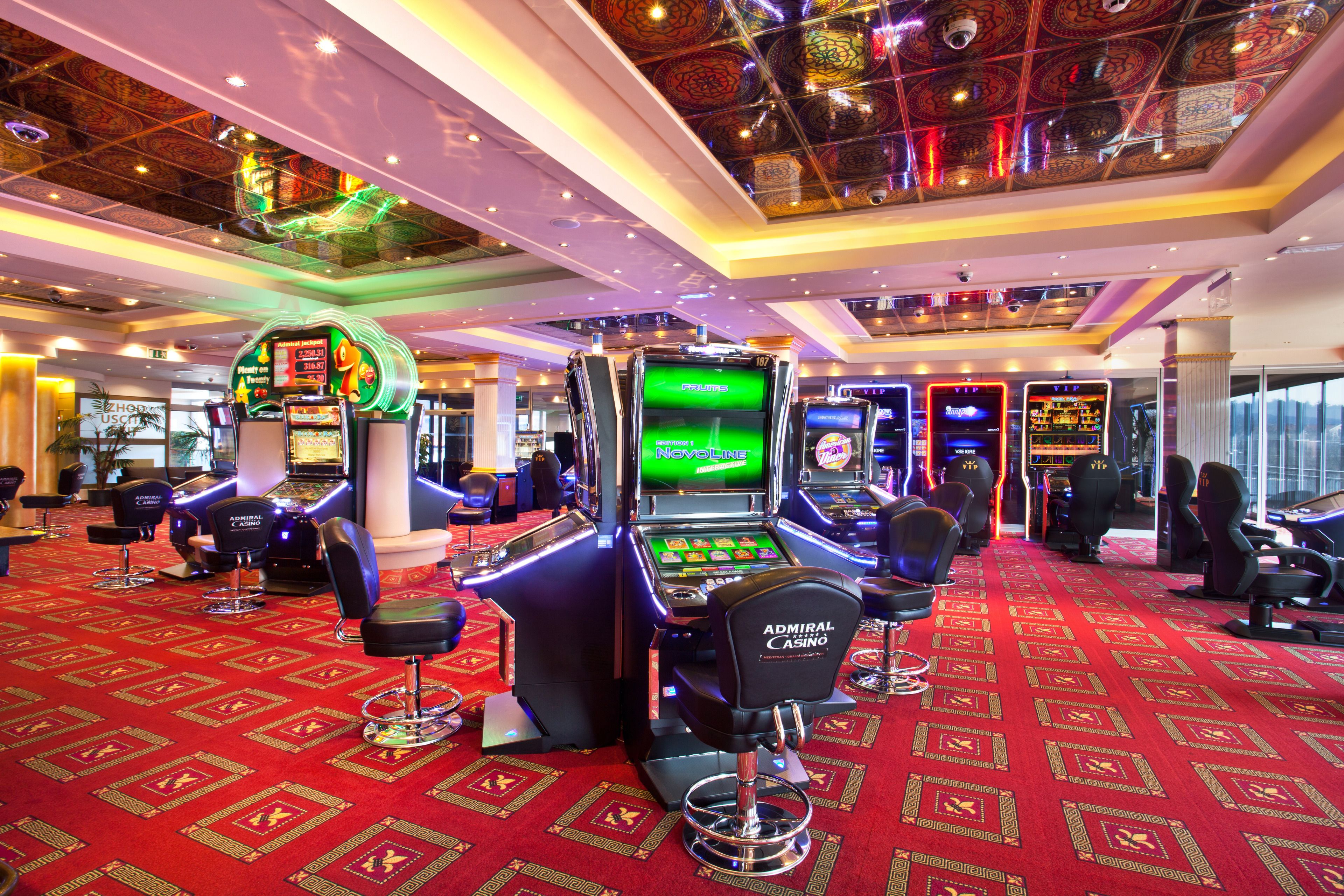 Un casinò con diverse slot machine, sgabelli da bar e un pavimento ricoperto di tappeto rosso.