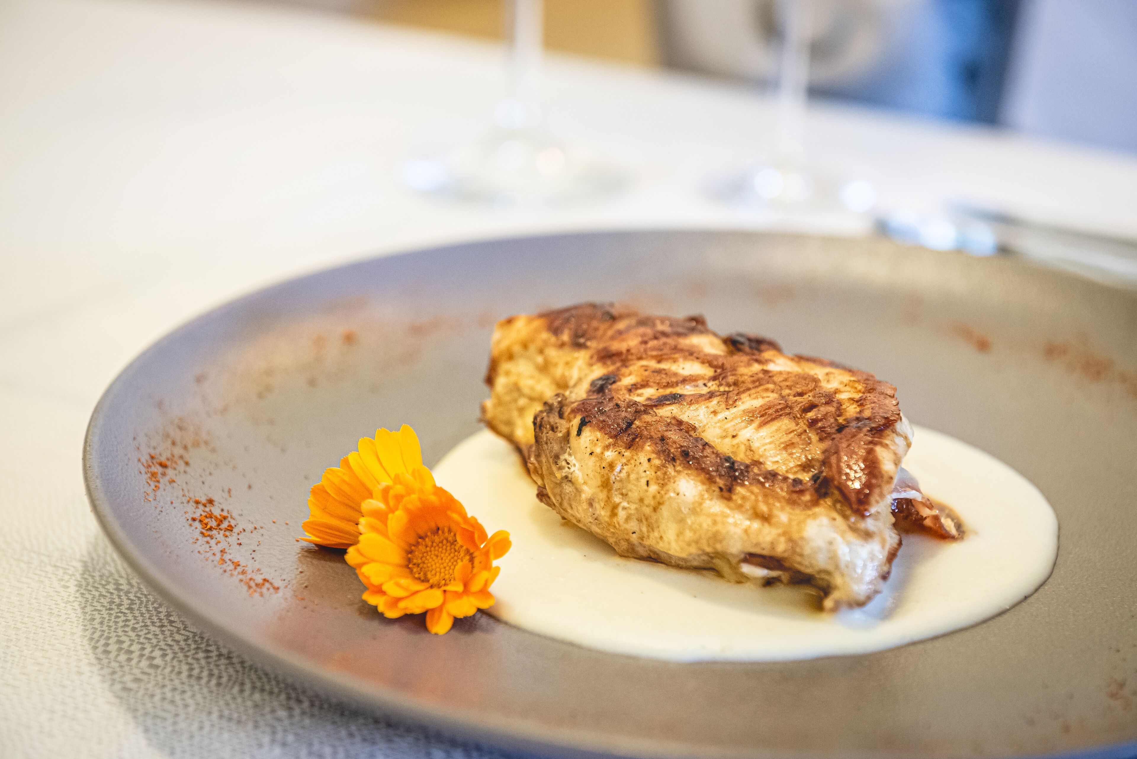 Un plato con pescado a la parrilla y una flor sobre una mesa.