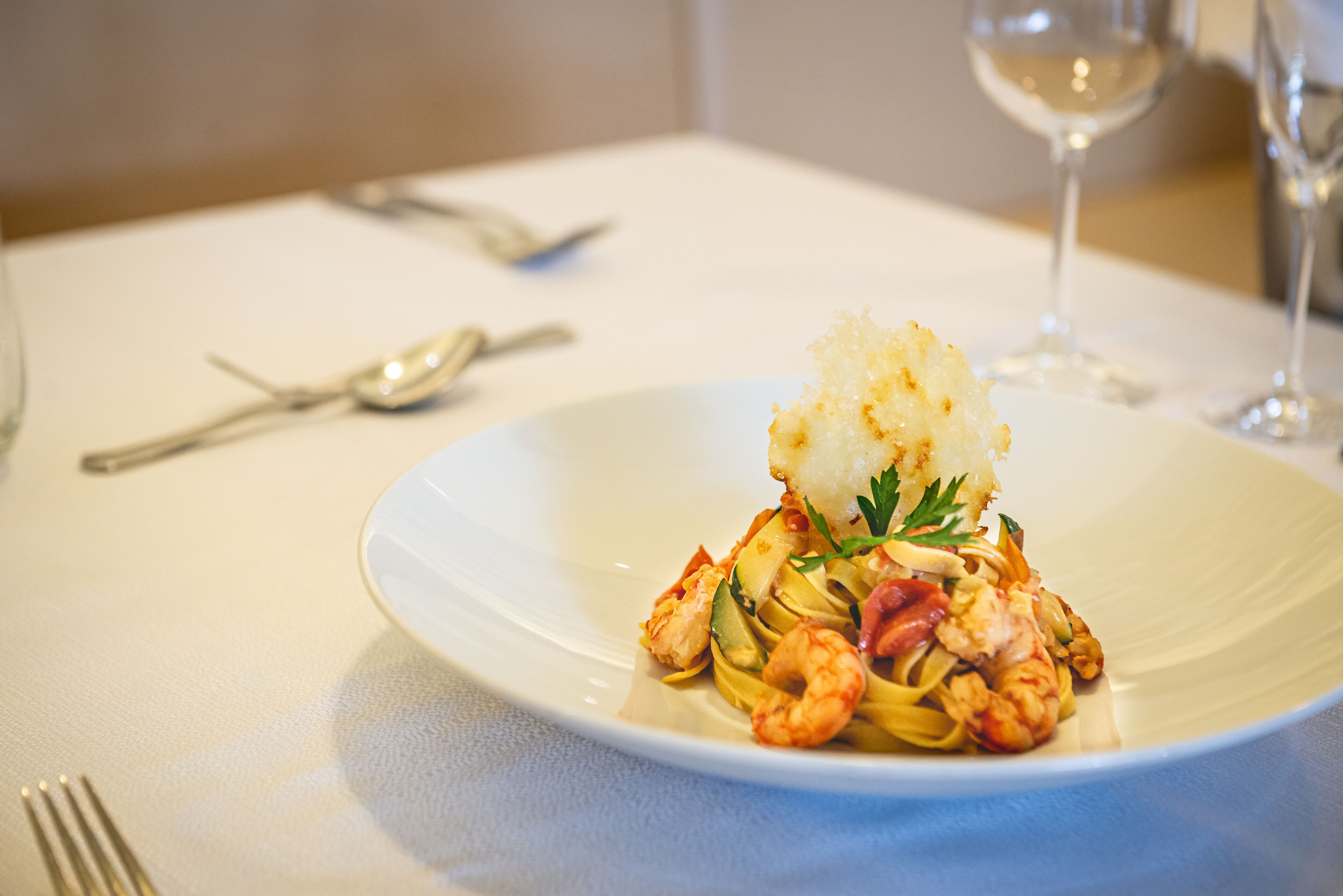 A plate of pasta with shrimp and a piece of bread on a white tablecloth.