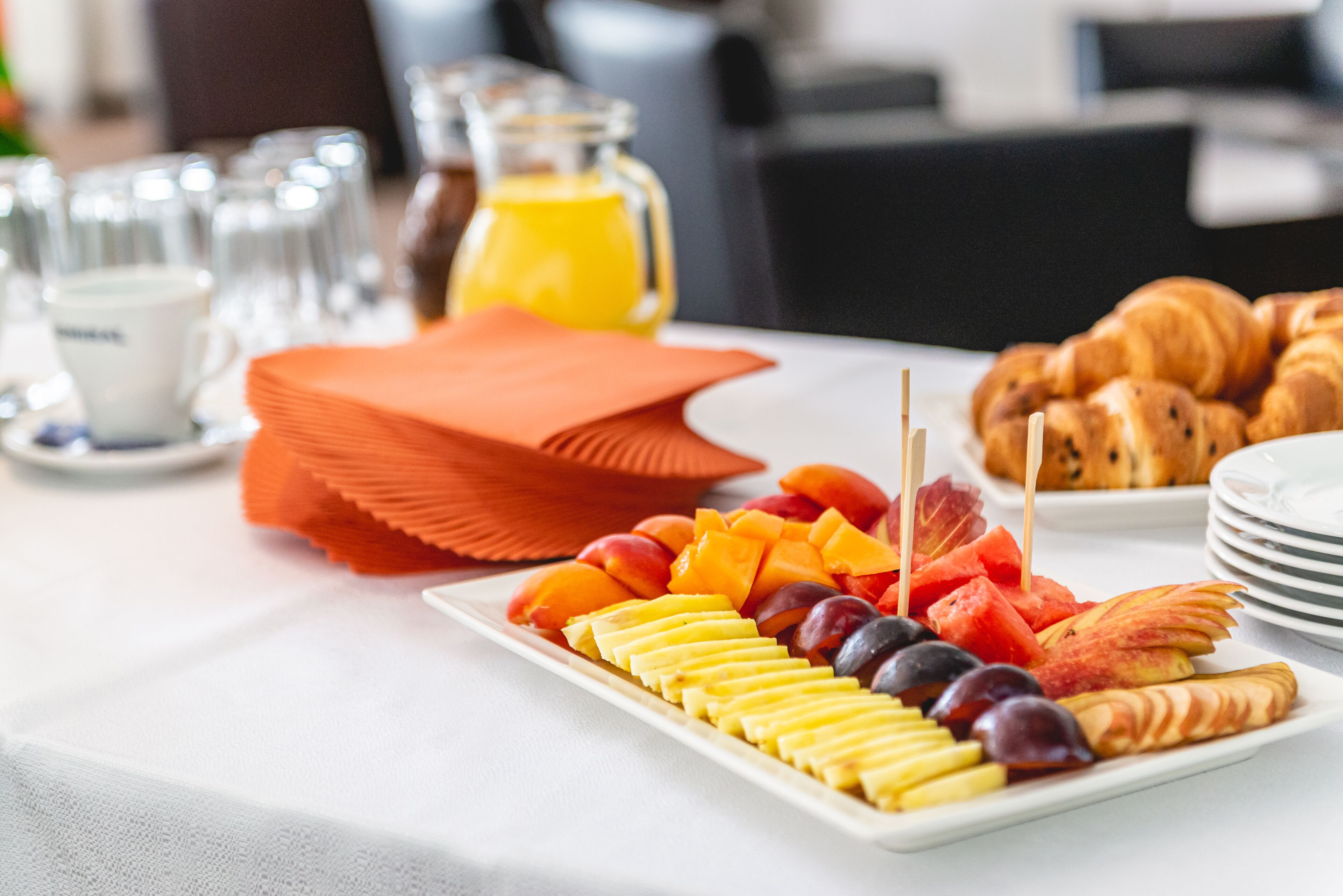 A breakfast buffet with fruits, pastries, and a coffee station.
