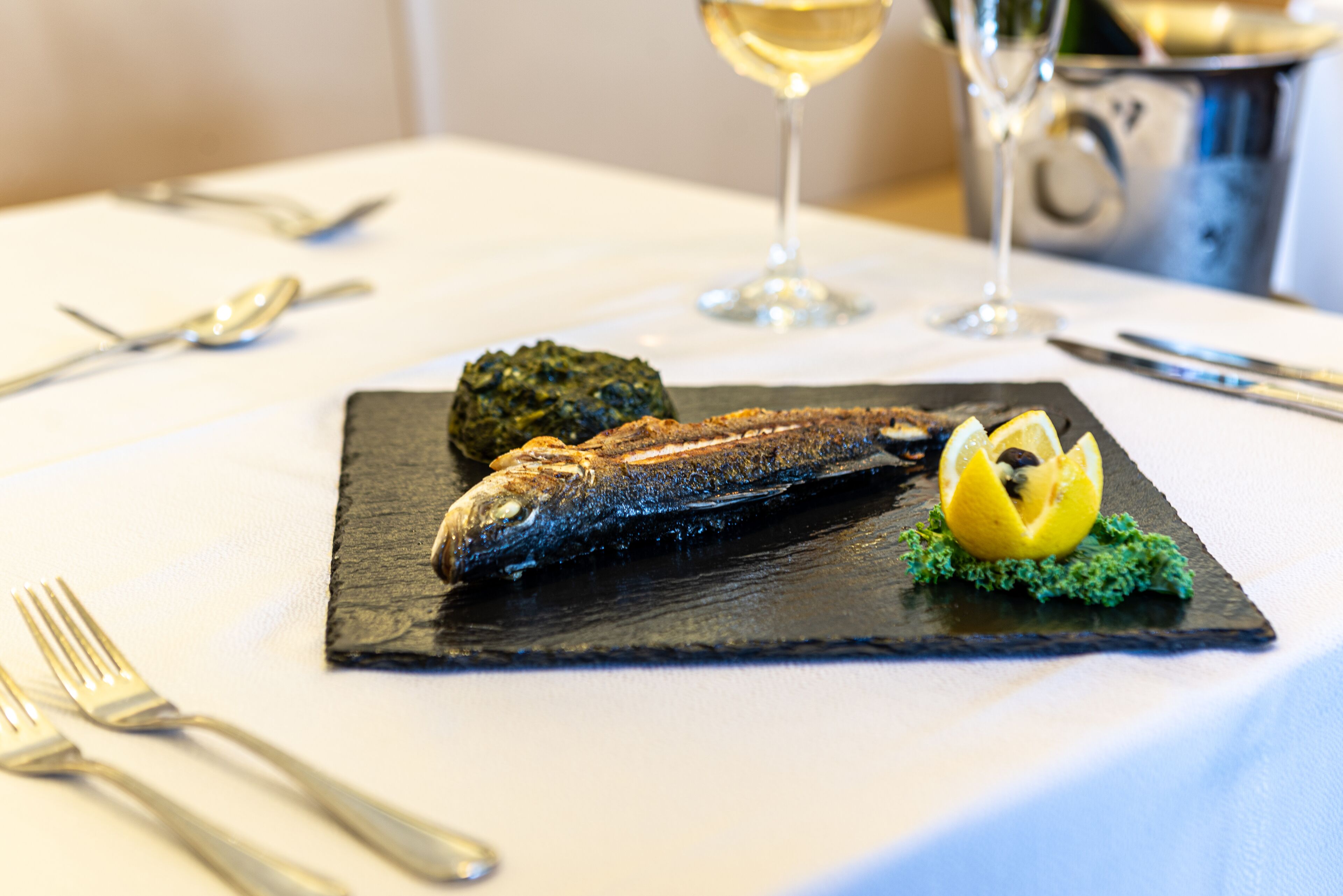 A dining table with a fish dish, a wine glass, and cutlery.