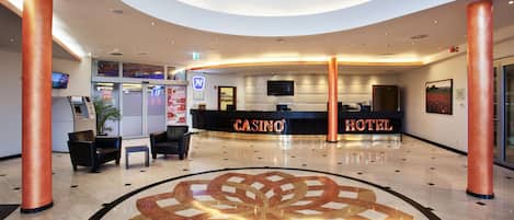 A lobby with a central circular design, a reception desk labeled 'CASINO HOTEL', and a seating area with chairs and a small table.