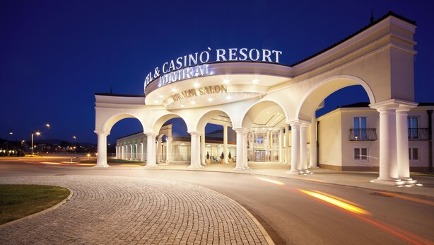 The exterior of the Hotel & Casino Resort with a prominent sign, a paved entrance, and a series of arches. - Casino & Hotel ADMIRAL Kozina (Hrpelje-Kozina)