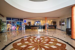 A spacious lobby with a central circular mosaic floor design, a reception desk labeled 'CASINO' and 'HOTEL', and a 'CASINO' sign above the desk.