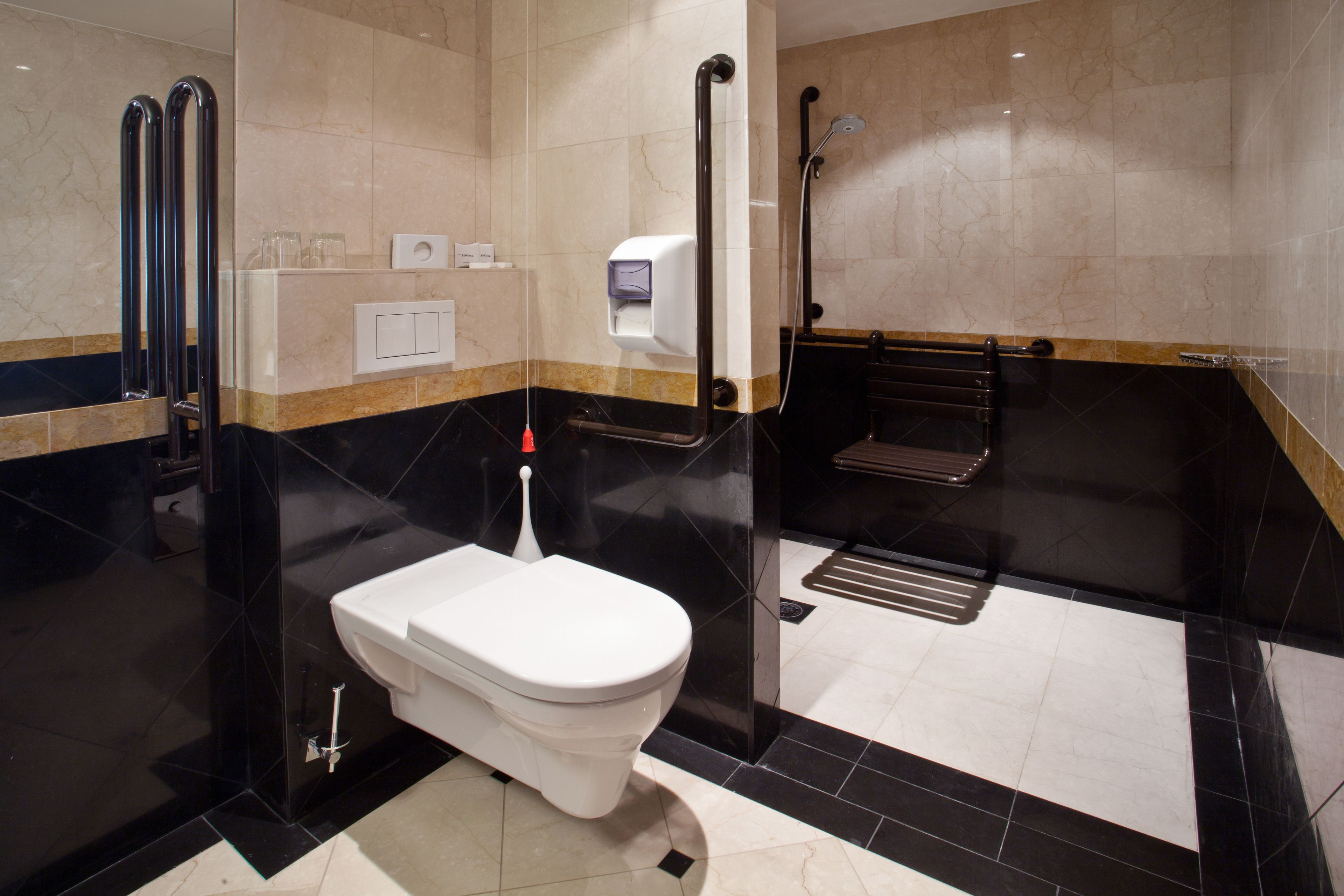 Un baño moderno con inodoro blanco, secador de manos, toallero y zona de ducha.