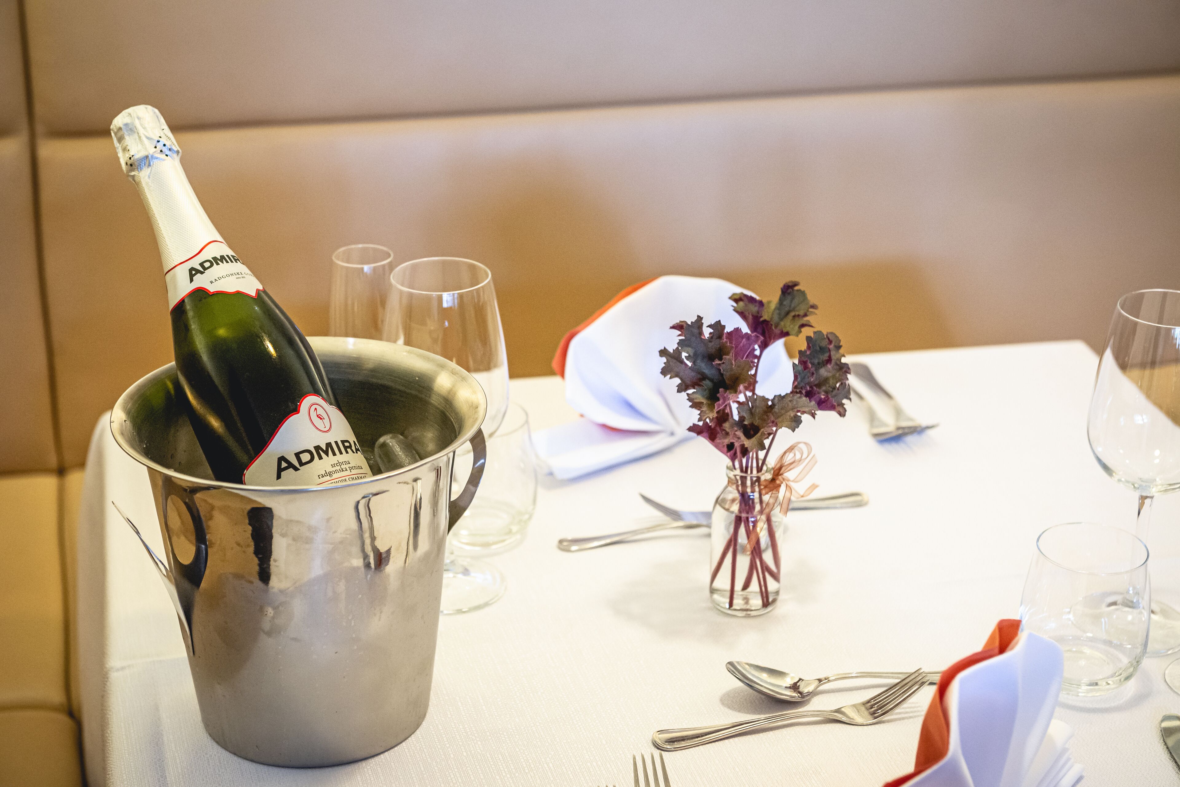 A dining table set with a champagne bottle in a metal bucket, a small vase with flowers, and neatly arranged cutlery.