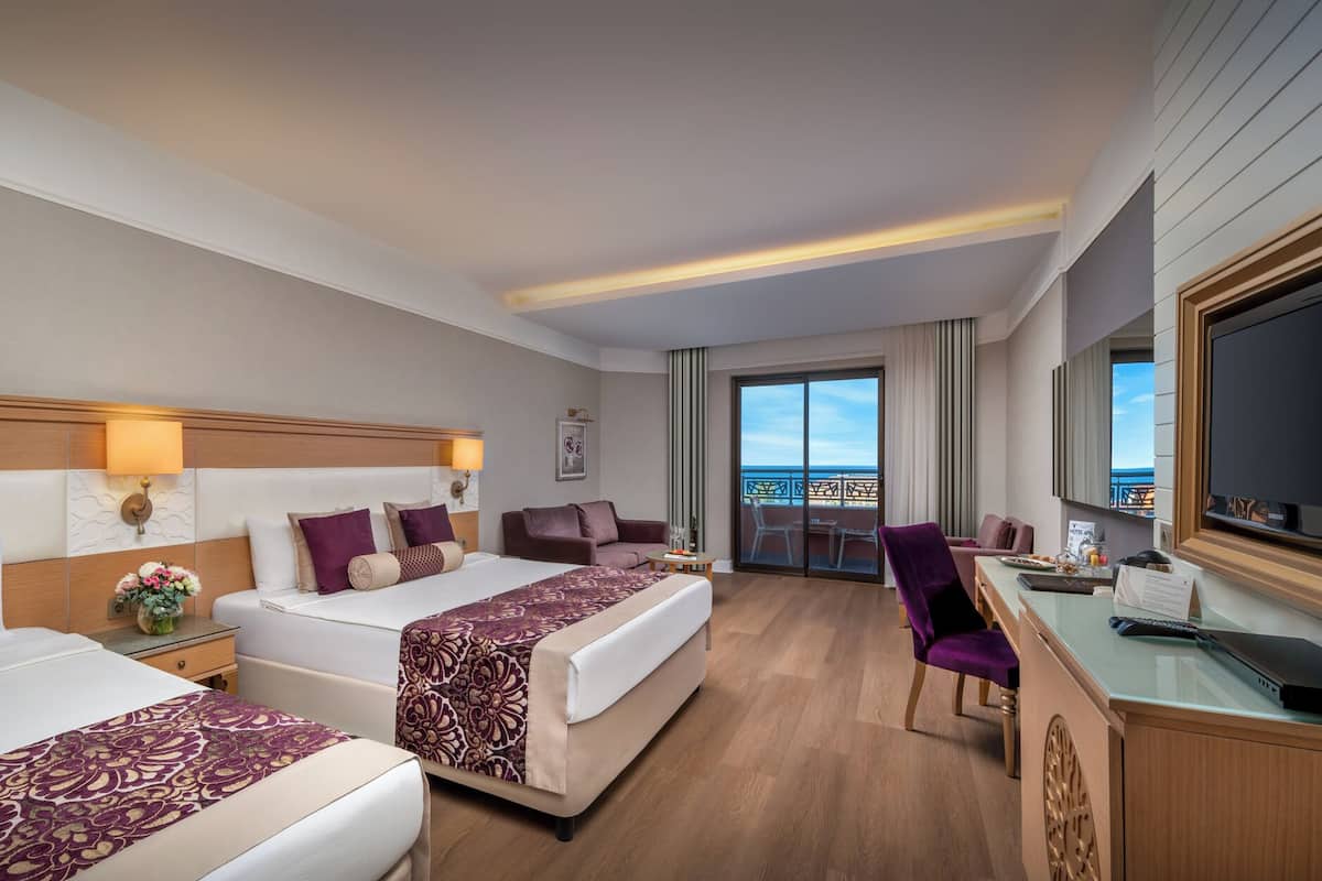 A hotel room with two beds, a desk, a TV, and a balcony with a view.