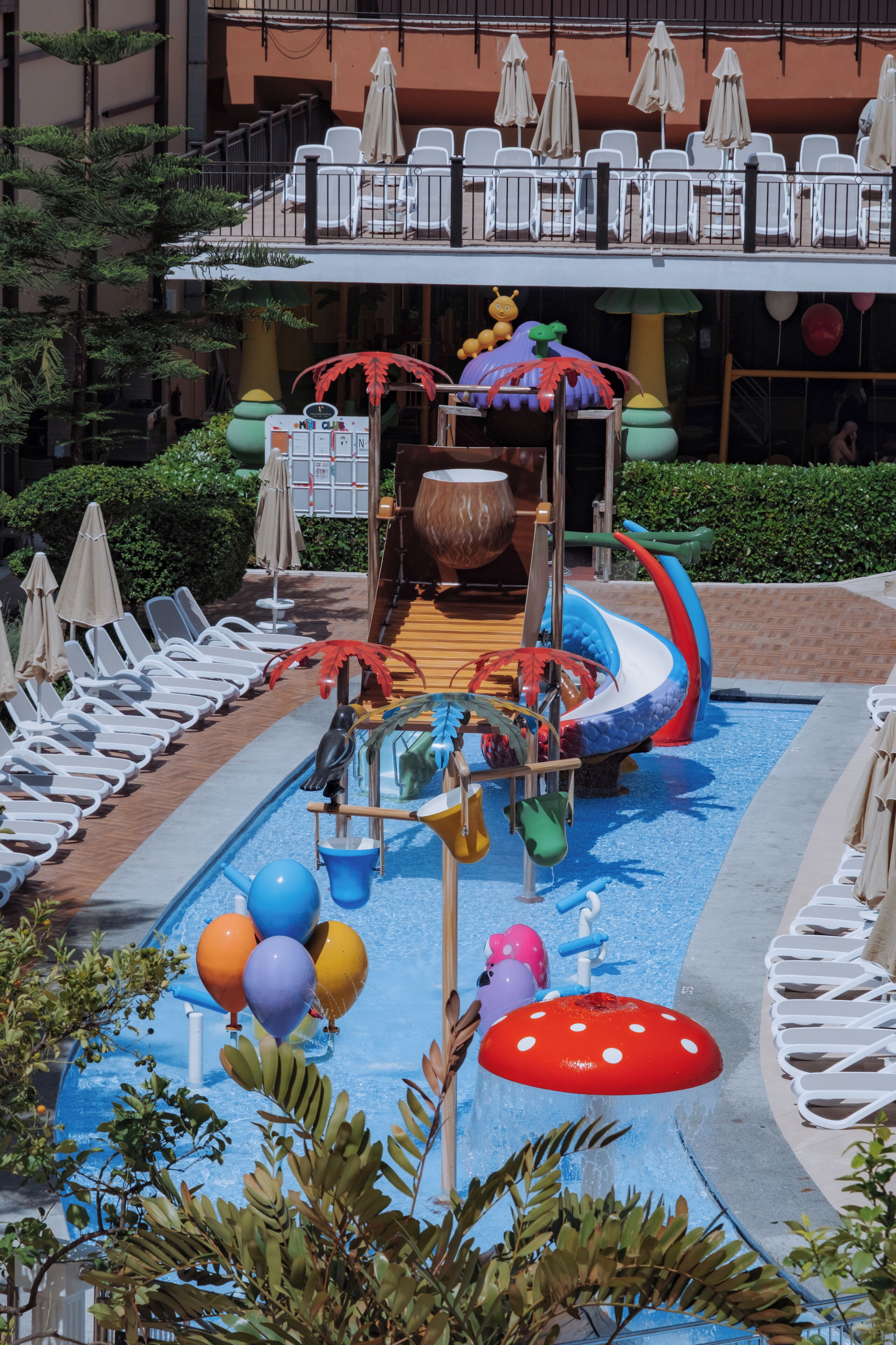 Uma área de piscina com espreguiçadeiras, um toboágua e um espaço de recreação infantil.