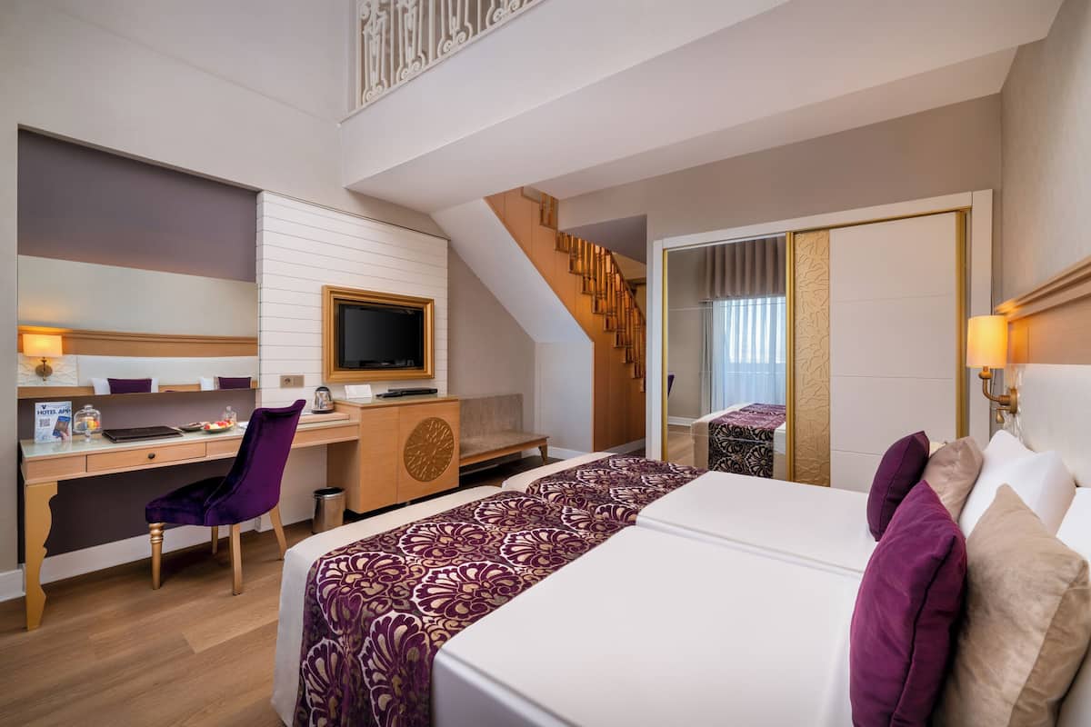 A hotel room with a bed, desk, chair, TV, and a staircase.