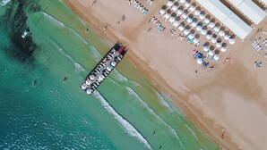 Luchtbeeld van een strand met een pier, strandparasols en ligstoelen.