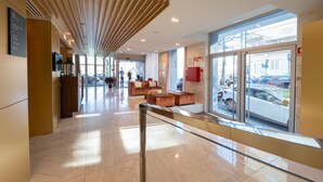 Um lobby moderno com guarda-corpo de vidro, teto de ripas de madeira e área de estar com sofás.