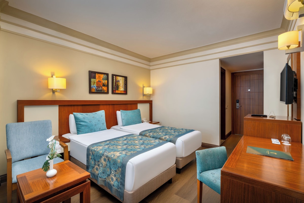 Une chambre d’hôtel avec deux lits, un bureau, une chaise et un téléviseur.