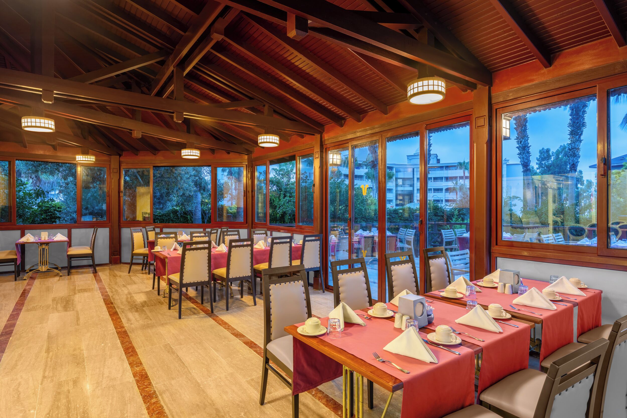 Un restaurante con varias mesas dispuestas para comer, amplios ventanales y techo de madera.