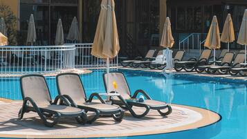 Uma área à beira da piscina com espreguiçadeiras e guarda-sóis.