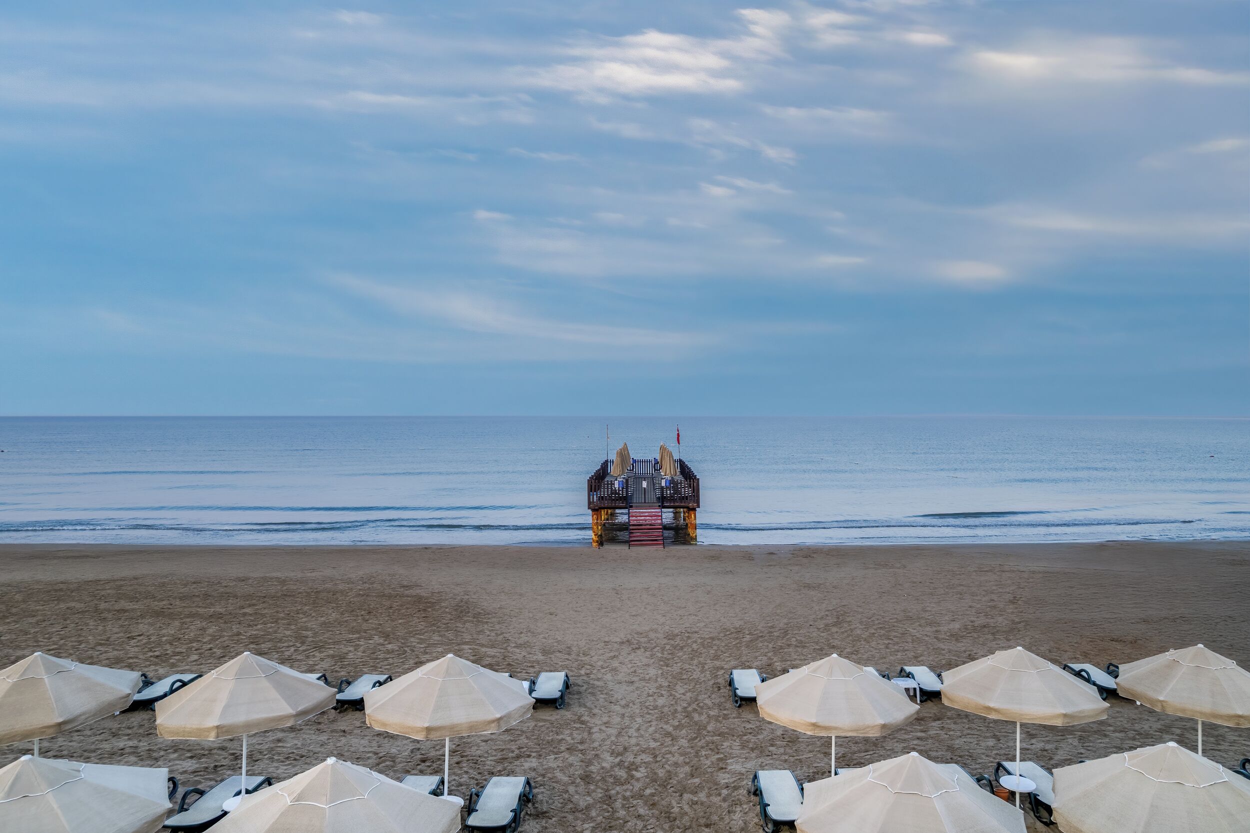 A beach with umbrellas and lounge chairs, a lifeguard tower, and the ocean.