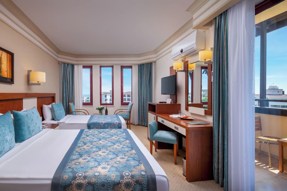 Habitación de hotel con dos camas, un escritorio, una silla, un televisor y ventanas amplias.