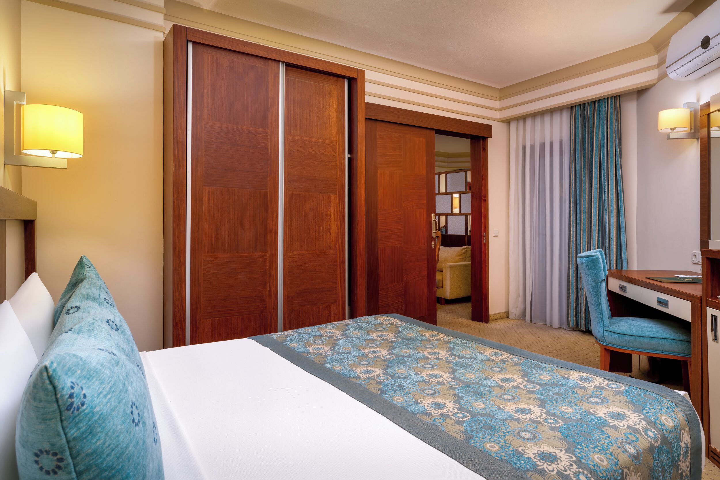 Habitación de hotel con cama, escritorio, silla, armario y baño visible a través de una puerta abierta.