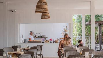 Un restaurante con un mostrador central, lámparas colgantes de mimbre y vistas al exterior.