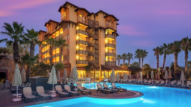 A hotel with a swimming pool, lounge chairs, and palm trees. - Villa Side Hotel (Manavgat)