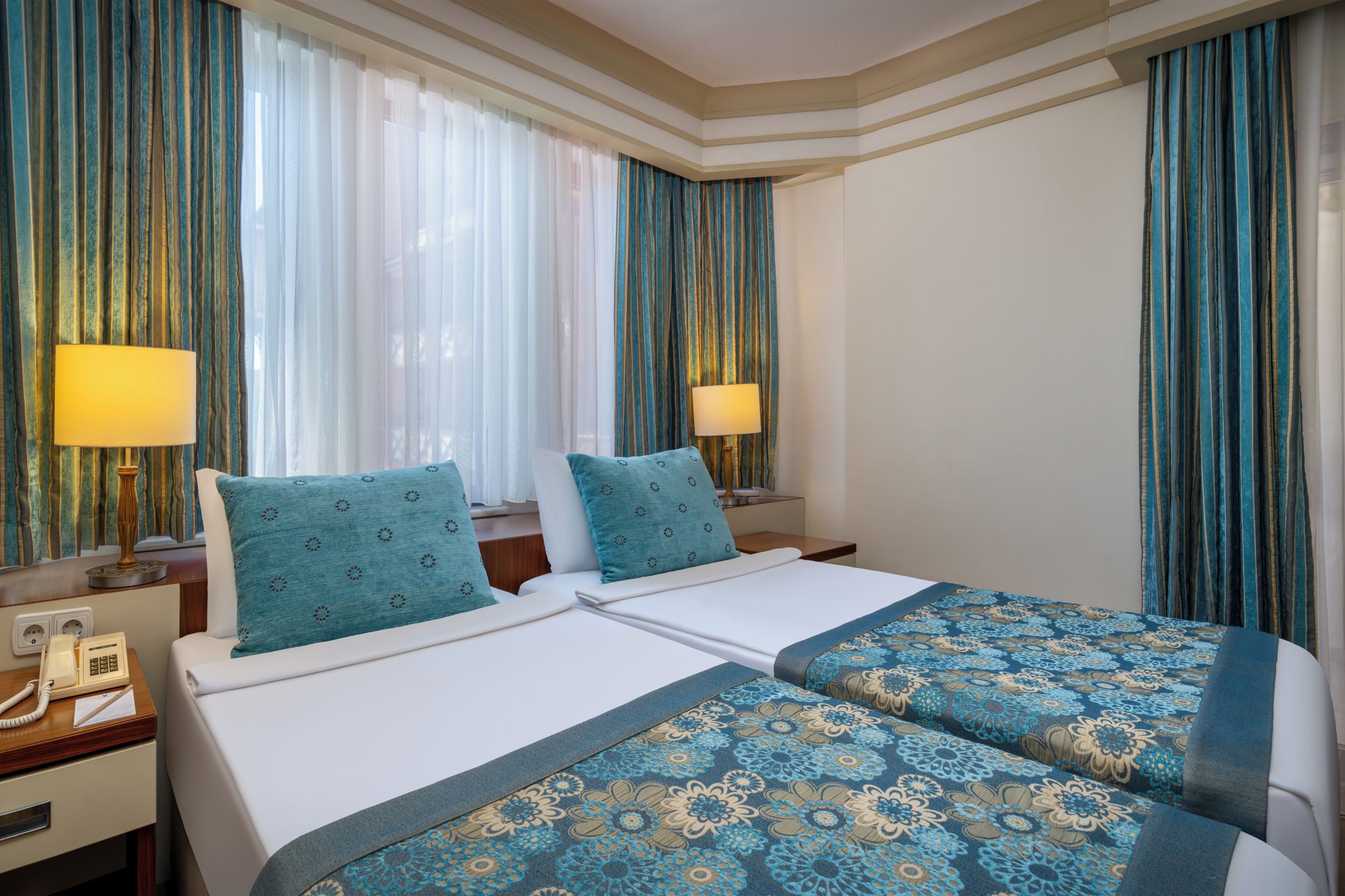 Habitación de hotel con dos camas, un escritorio y teléfono, y cortinas.