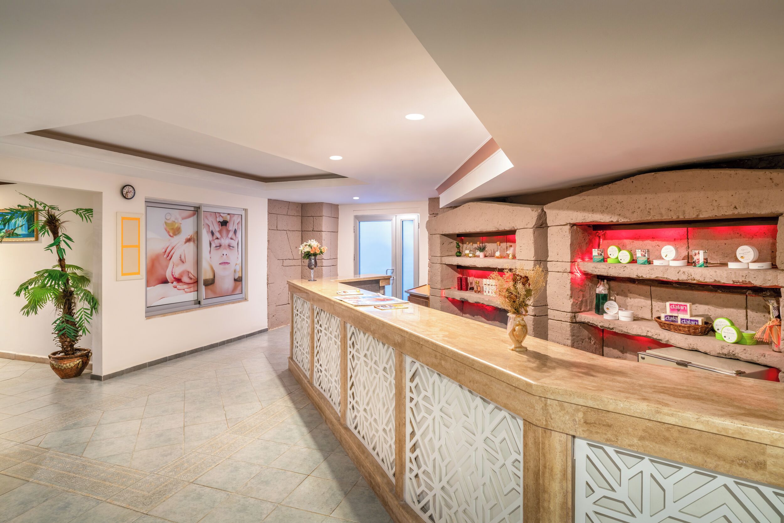 A reception area with a counter, decorative wall panels, a potted plant, and a window.