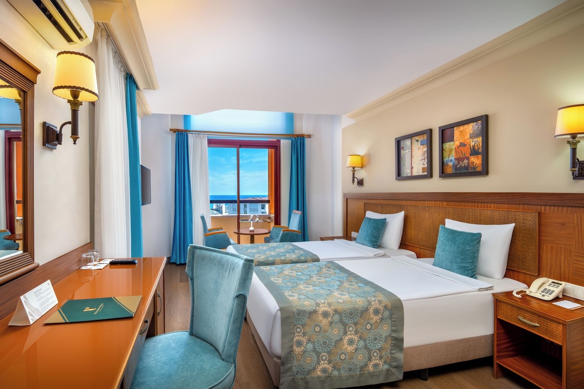 Une chambre d’hôtel avec un lit, deux chaises, un bureau, un téléphone et une fenêtre donnant sur un paysage agréable.