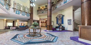 Un vestíbulo espacioso con una mesa redonda central, una recepción y una escalera con barandales decorativos.