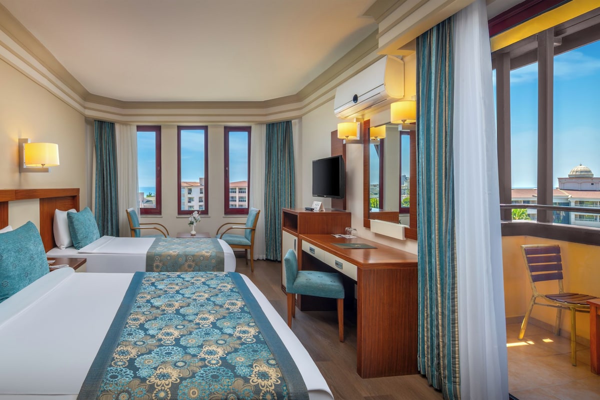 Une chambre d’hôtel avec deux lits, un bureau, une télévision et de grandes fenêtres donnant sur des immeubles.