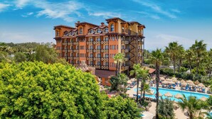 A multi-story hotel with a pool, surrounded by palm trees and greenery. - Villa Side Hotel (Manavgat)