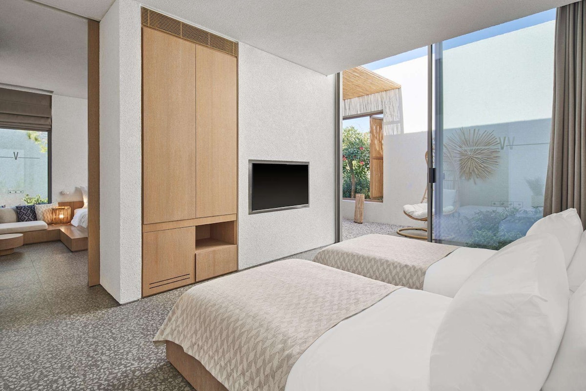 Ein modernes Schlafzimmer mit einem großen Schiebeglasfenster zum Balkon, einem eingebauten Fernseher und einer gemütlichen Sitzecke mit Sofa und Sessel.