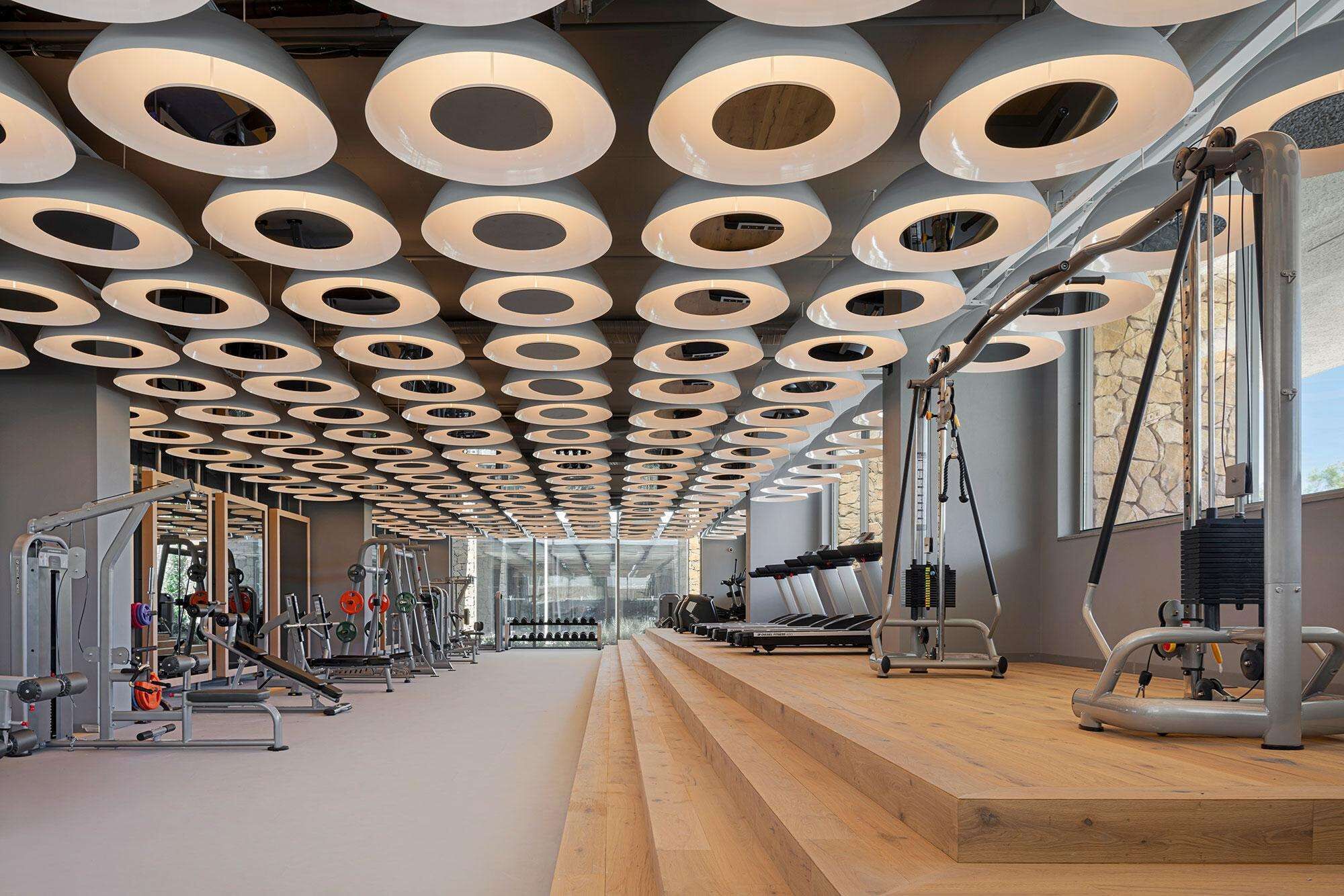 A gym with a unique ceiling design featuring circular patterns and various exercise equipment.