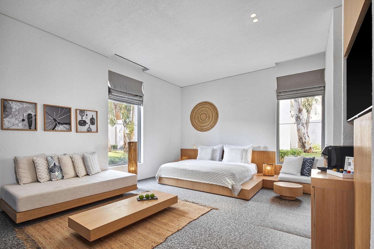 Ein modernes Schlafzimmer mit einem großen Bett, einer Couch, einem Couchtisch und Kunstwerken an den Wänden.