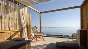 Une terrasse en bois avec un canapé, un fauteuil en osier et une petite table, donnant sur une étendue d’eau calme.