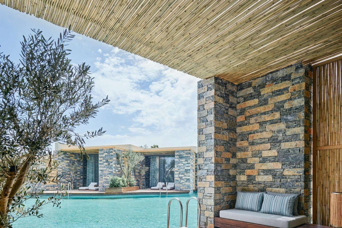Ein Poolbereich mit Holzliegen, einer Steinmauer und Blick auf einen Pool.
