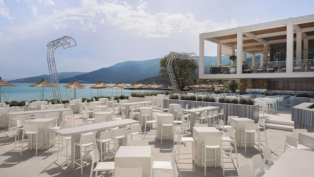 An outdoor seating area with white tables and chairs, overlooking a body of water and mountains. - Voyage Torba (Bodrum)