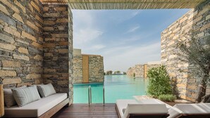 A stone-walled infinity pool with a wooden deck, a cushioned seating area, and lounge chairs. - Voyage Torba (Bodrum)