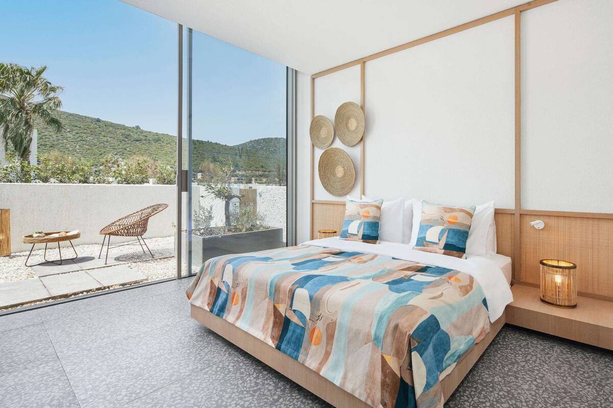 Ein modernes Schlafzimmer mit einem großen Bett, Blick ins Freie und einem Balkon mit Sitzgelegenheiten.