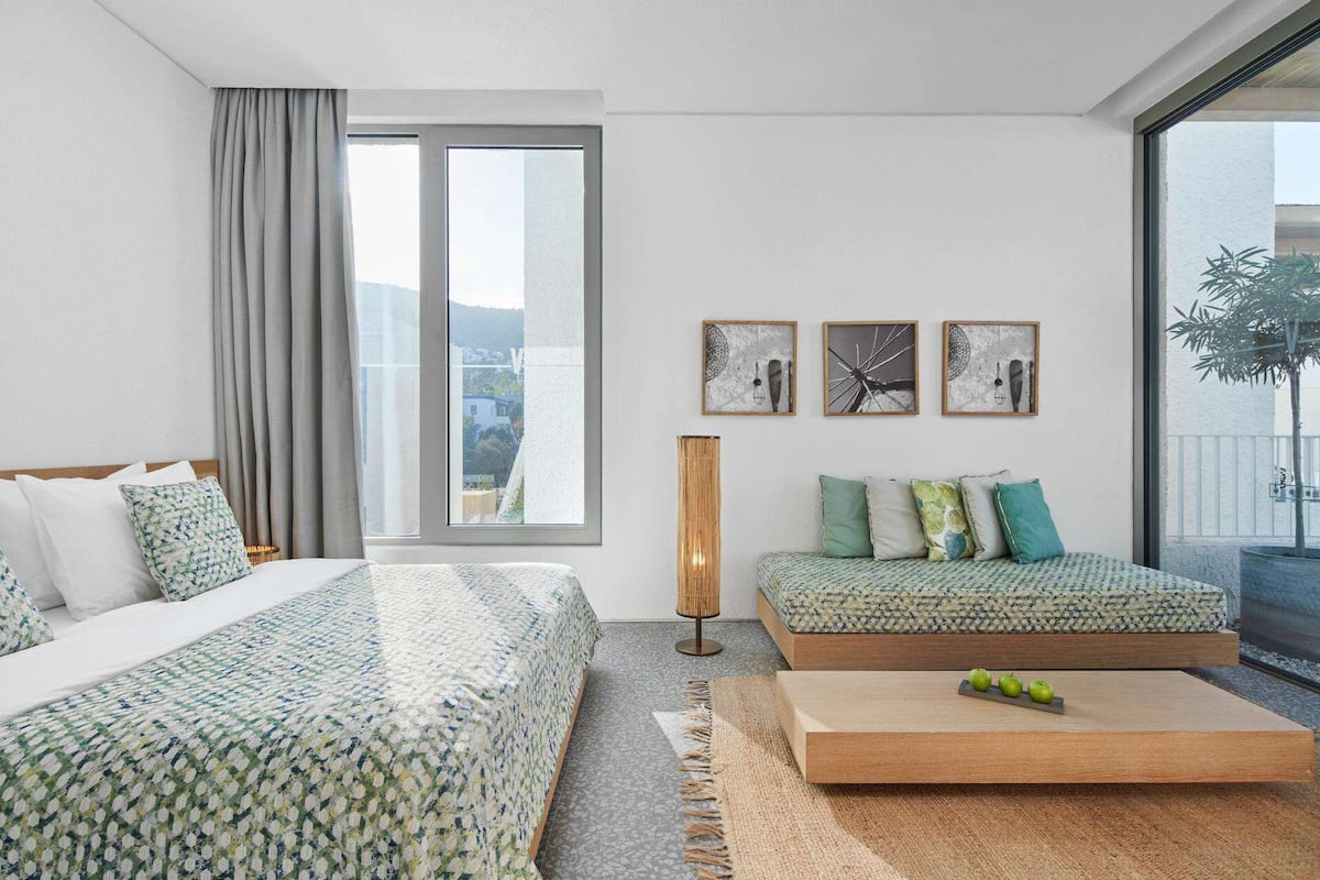 Ein modernes Hotelzimmer mit großem Fenster, einem Bett, einer Couch und einem kleinen Tisch mit Äpfeln.