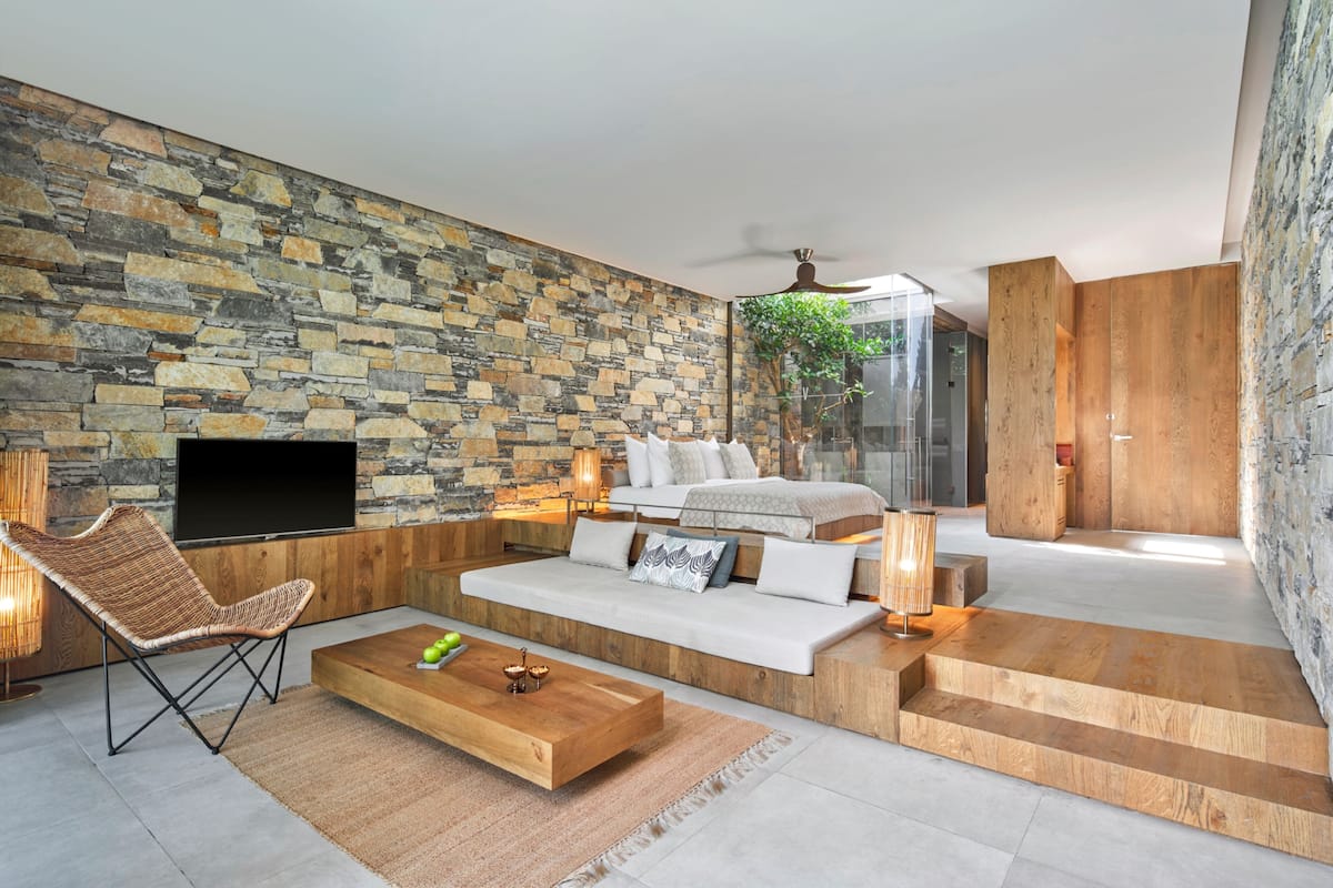 Ein modernes Wohnzimmer mit Steinwand, einer Couch, einem Couchtisch, einem Fernseher und einer Treppe, die zu einer Holztür führt.
