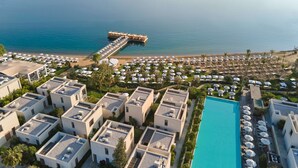 Un resort con varias edificaciones, una piscina y un muelle que se adentra en el mar.
