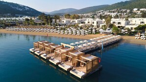 Un hotel frente al agua con habitaciones de terraza de madera, una playa y vistas del pueblo en la colina.