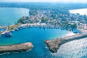 Vista aérea de un pueblo costero con un puerto deportivo, rompeolas rocosas y edificios residenciales.