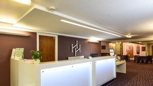 Un espace d’accueil comprenant un comptoir de réception, une plante en pot, un panneau fixé au mur et un tapis à motifs.