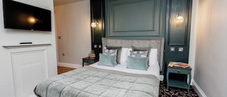 Un dormitorio con una cama grande, un televisor de pantalla plana montado en la pared y dos mesitas de noche con lámparas.