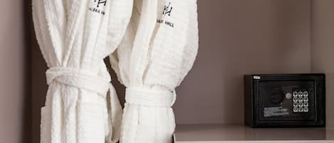 Two white bathrobes hanging on a rack, a black safe on a shelf, and a white cabinet.