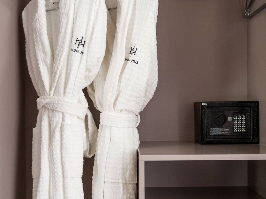 Deux peignoirs blancs sont suspendus à un porte-vêtements, un coffre-fort noir est posé sur une étagère, et il y a une armoire blanche.