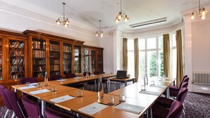Une salle de conférence avec une longue table, des chaises violettes, une bibliothèque et une grande fenêtre avec des rideaux.