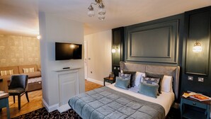 Une chambre d’hôtel moderne dotée d’un grand lit, d’une télévision à écran plat, d’un coin salon avec un canapé et un fauteuil, ainsi que d’une petite table.