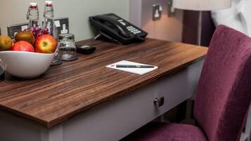 A hotel room desk with a bowl of fruit, a phone, and a pen.
