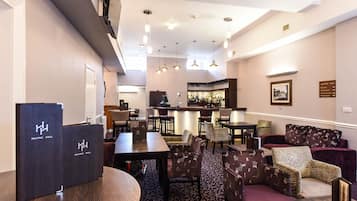Un hall de hotel con una zona de bar, distribución de asientos y un mostrador de recepción.